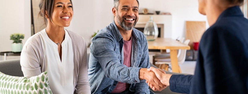 Happy smiling couple greeting broker with handshake at home