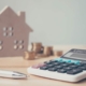 Calculator with wooden house and coins stack and pen on wood table